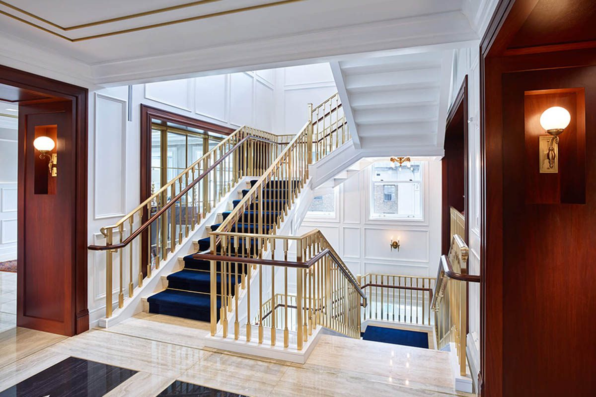 Elegant staircase with gold railings and blue carpet in a bright interior.