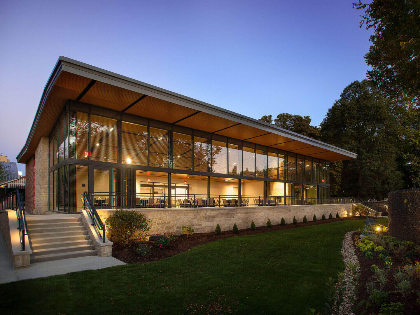 Modern house with large glass windows and warm interior lighting at dusk.