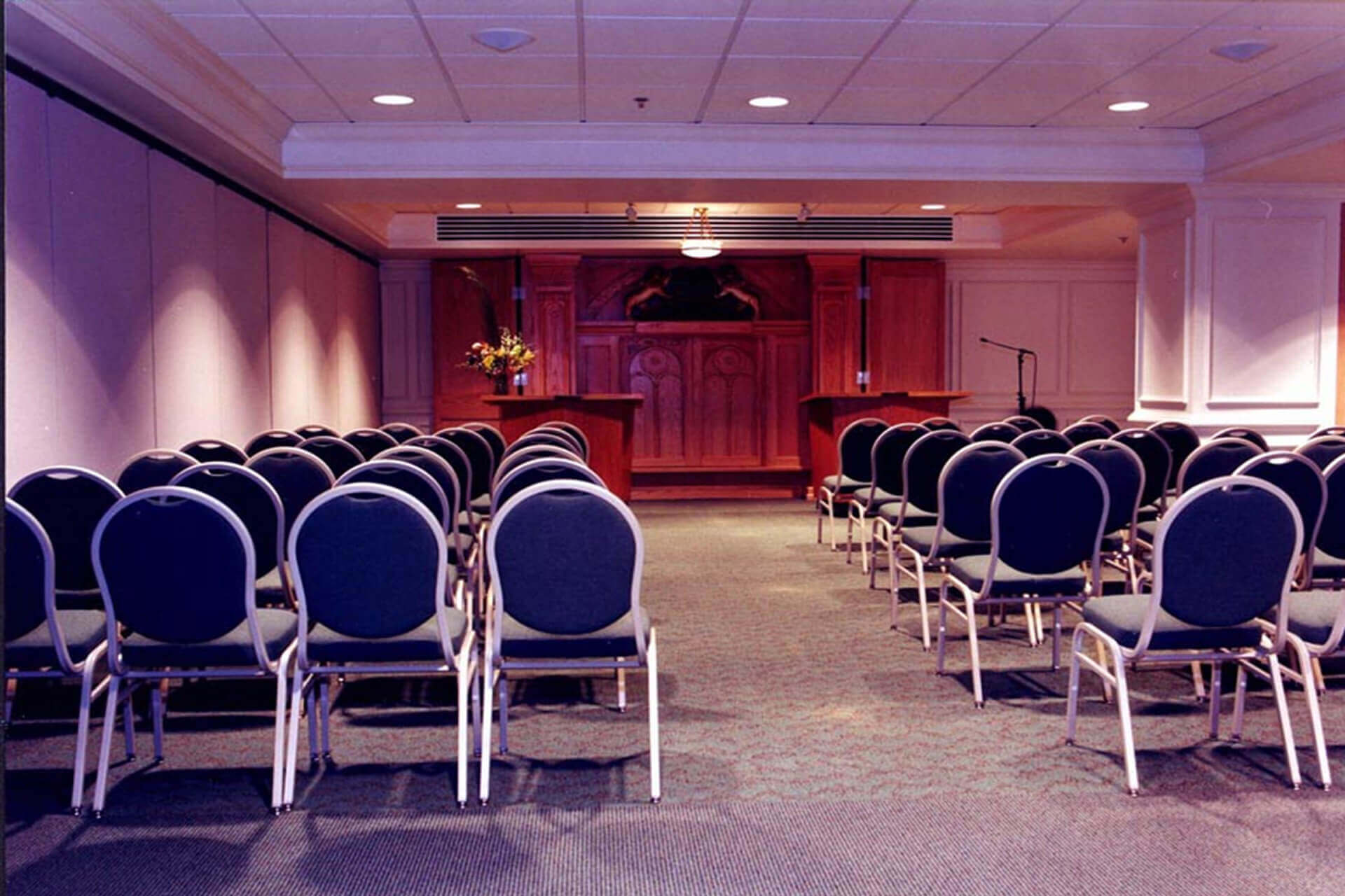 An empty conference room with rows of blue chairs and a podium at the front.