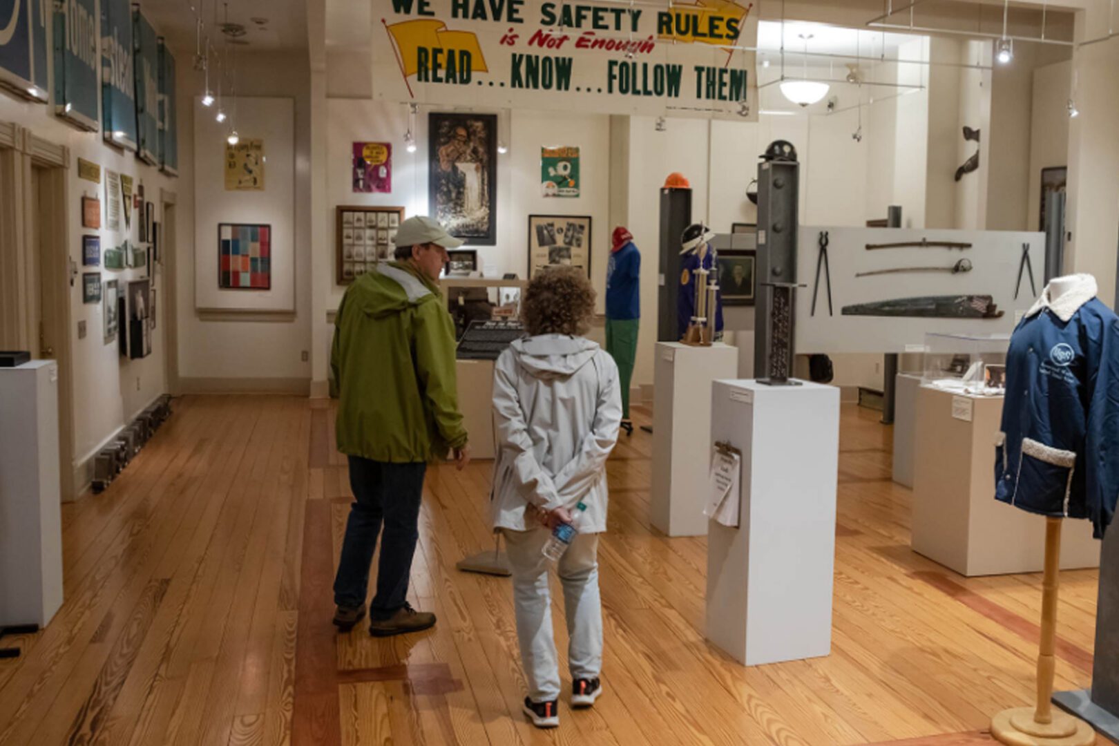 Two people observing artwork in a small gallery with safety rules posted.