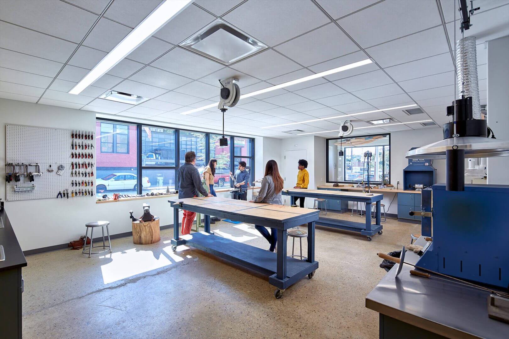 People working on projects in a bright, spacious workshop with large windows.
