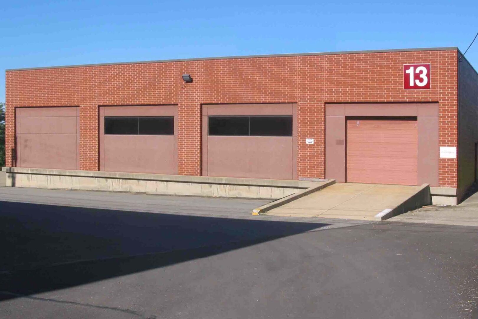 Three closed garage doors on a brick building under a clear blue sky.
