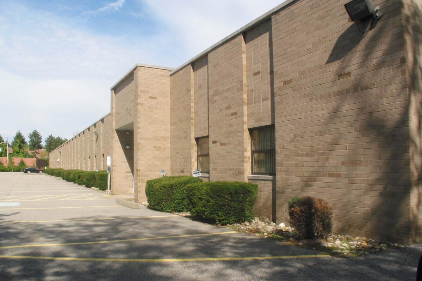Exterior view of a beige brick building with small windows and bushes.