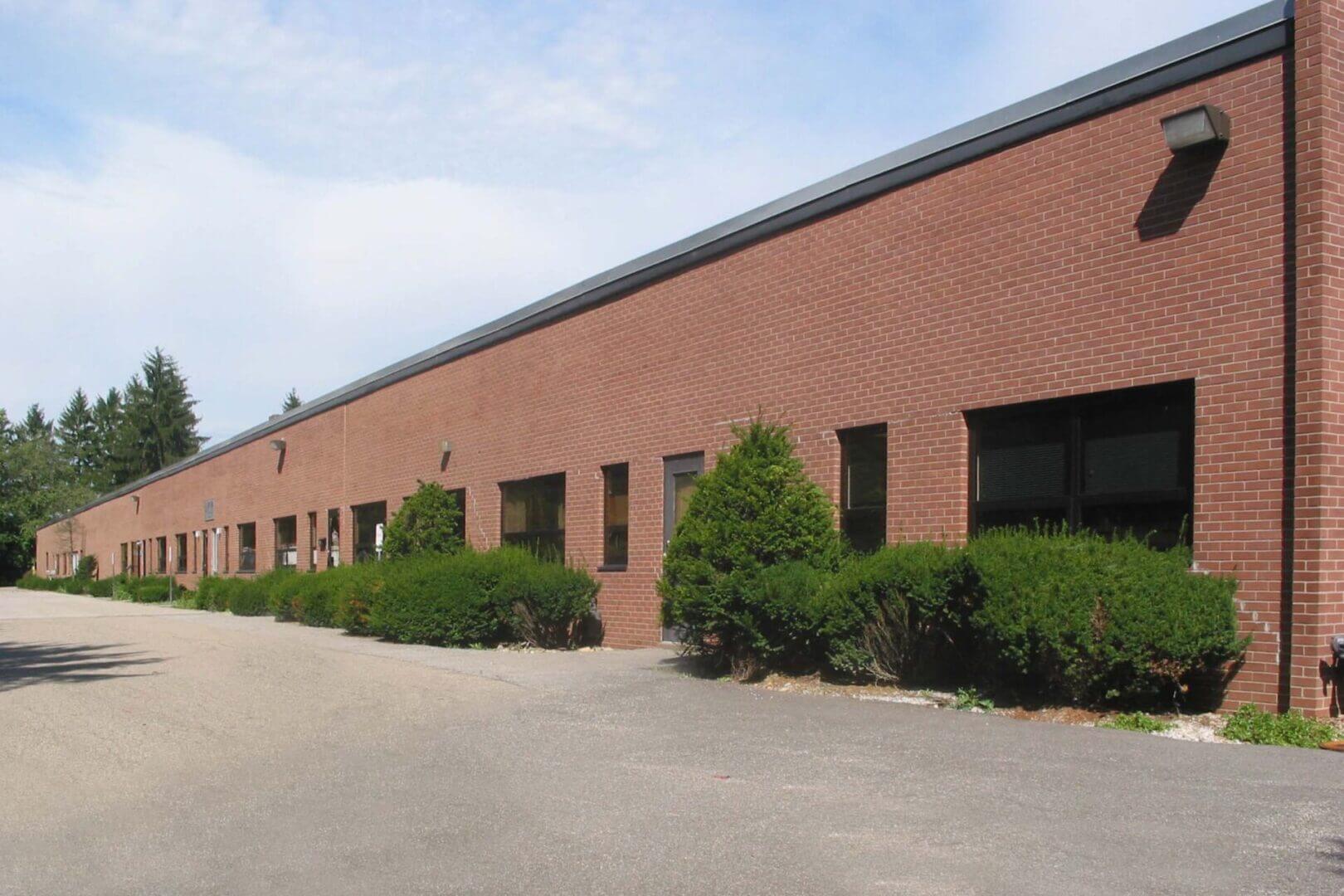 A long brick building with multiple windows and green bushes outside.