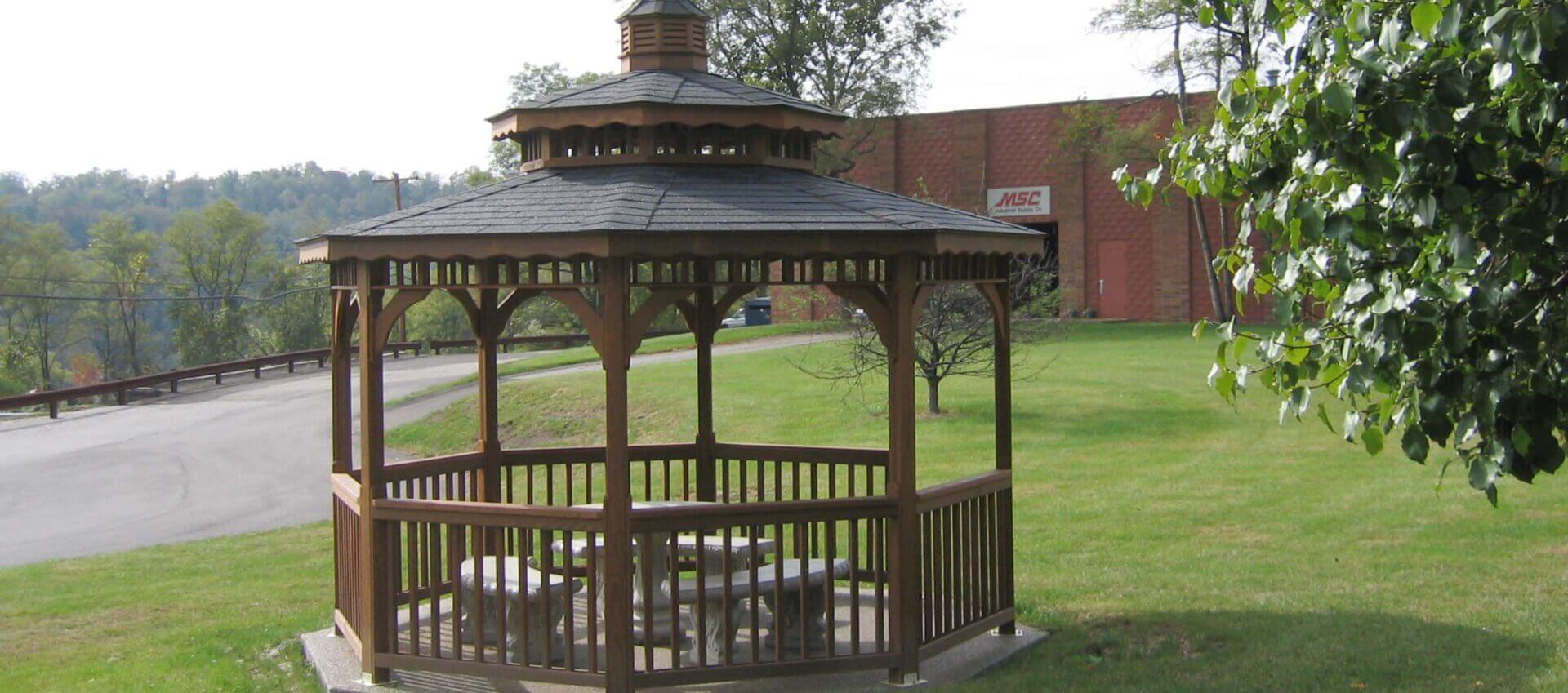 Wooden gazebo with benches in a grassy area.