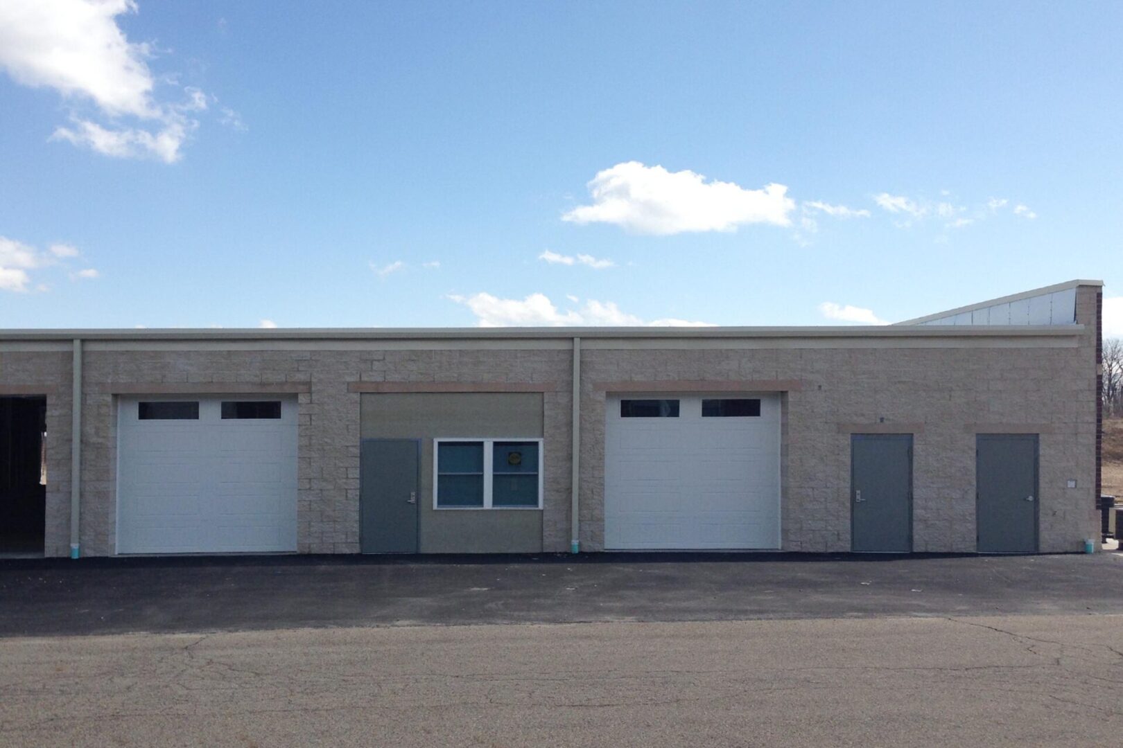 A white commercial building with two garage doors and a central window under a blue sky.