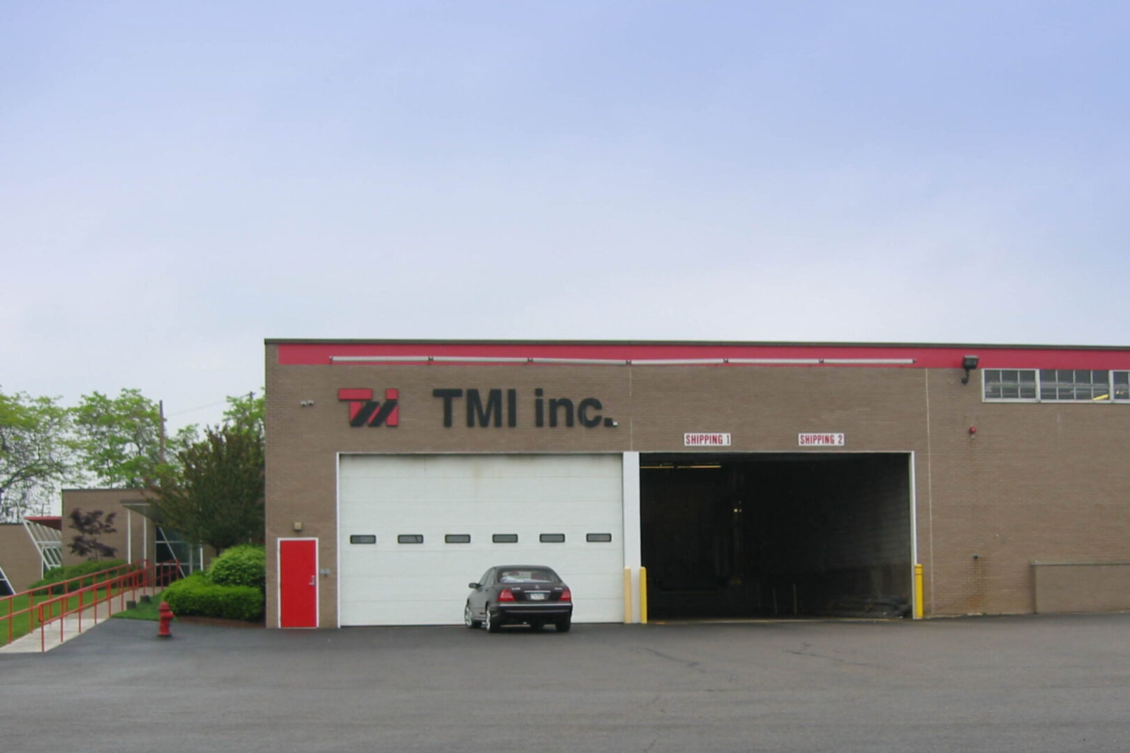 A car parked outside a TMI Inc. industrial building with large garage doors.