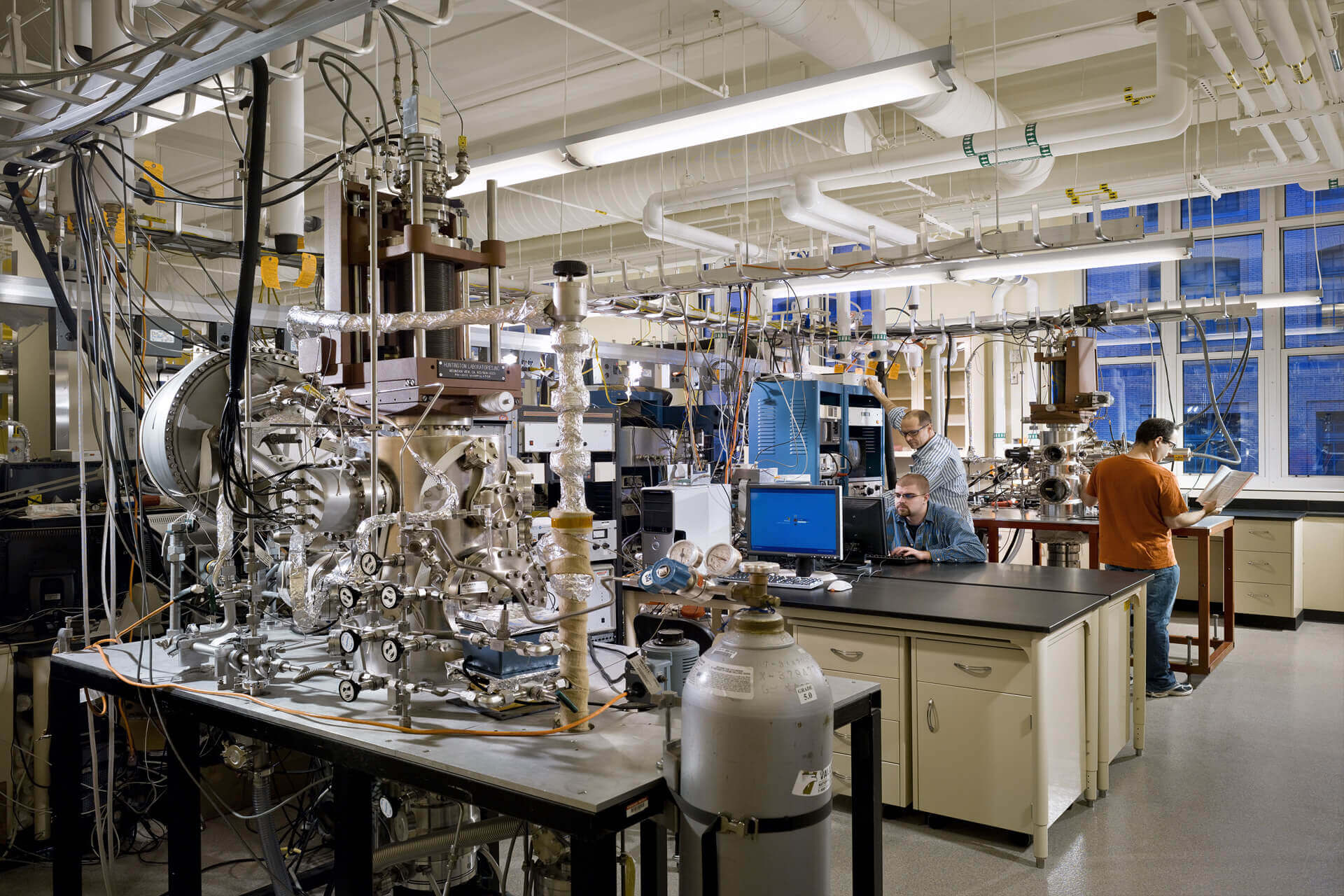 A scientist works in a complex laboratory filled with scientific equipment and pipes.