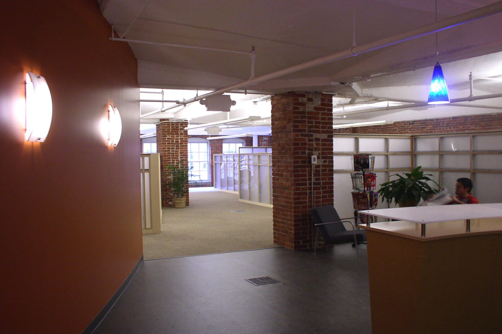 Interior view of a modern office hallway with brick pillars and glass partitions.