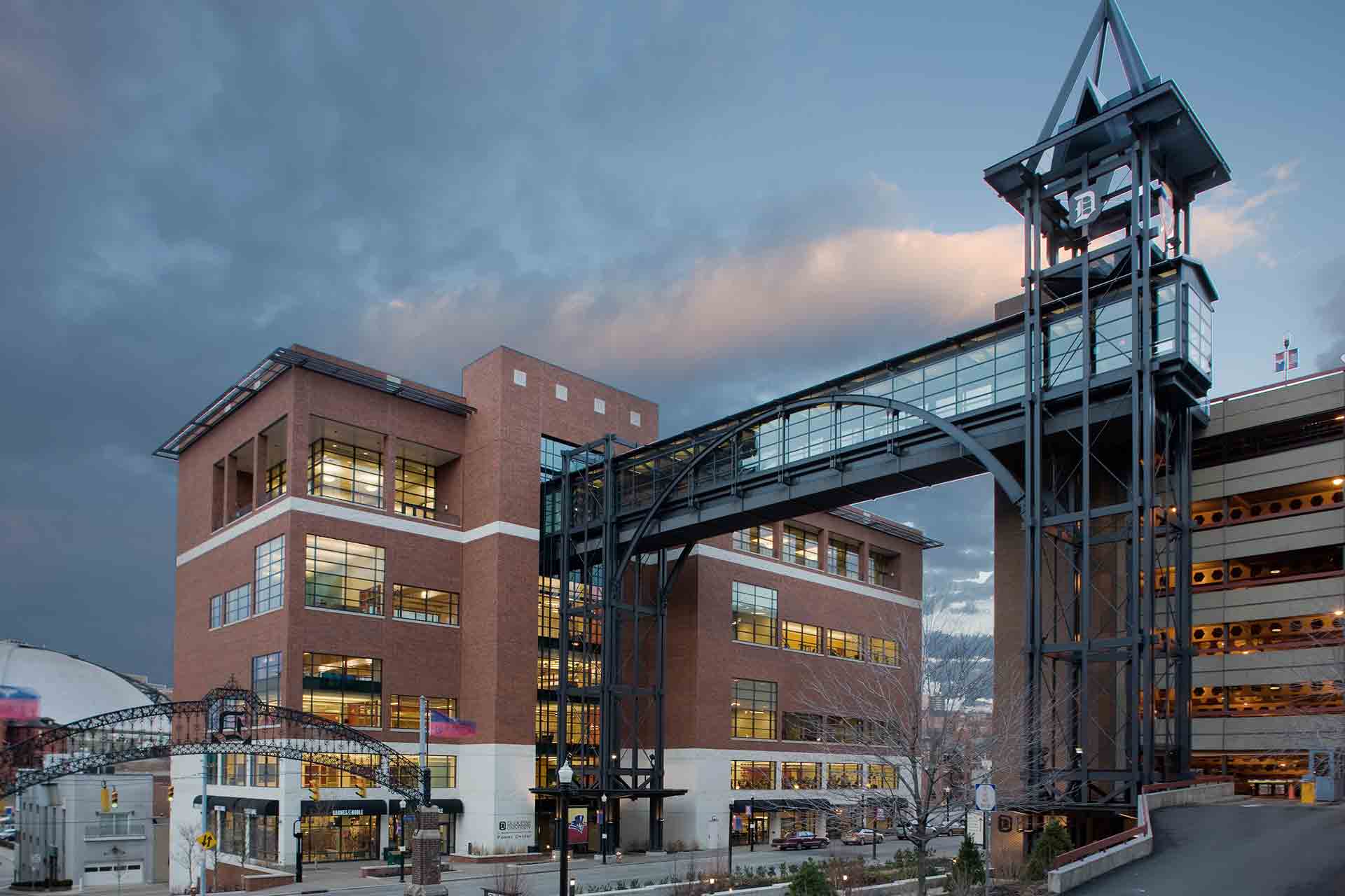 Industrial buildings connected by a glass skybridge at dusk.