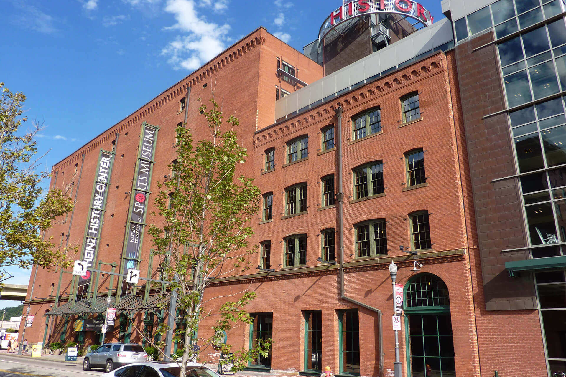 Red brick buildings with a tree and street signs in front on a sunny day.