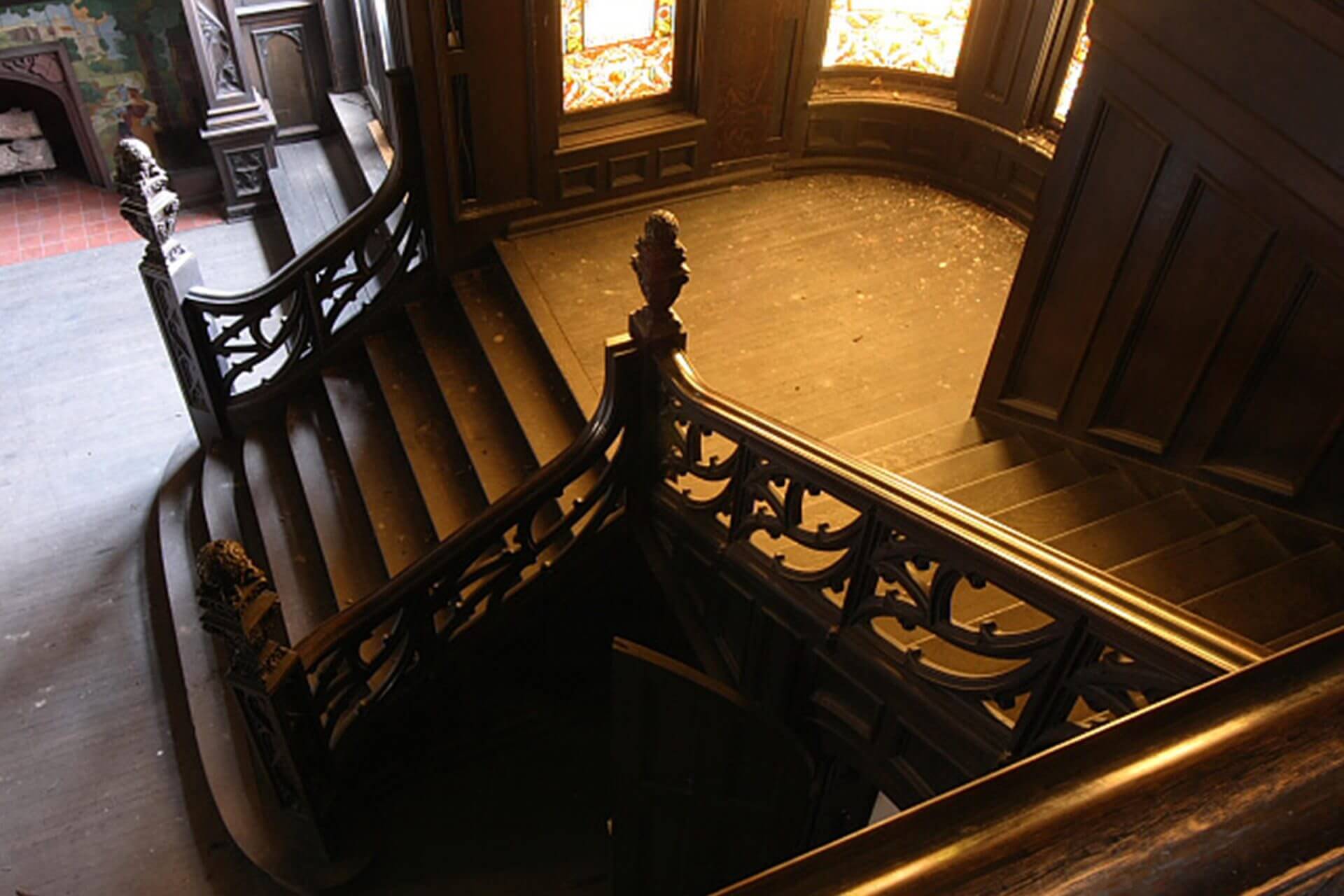 Ornate wooden staircase with detailed railing and stained glass windows.
