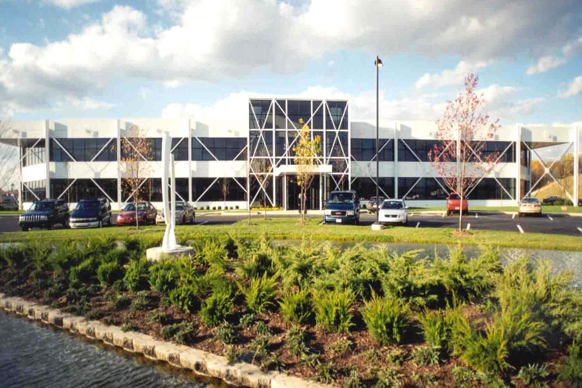 A parking garage with cars and green landscaping in front under a partly cloudy sky.