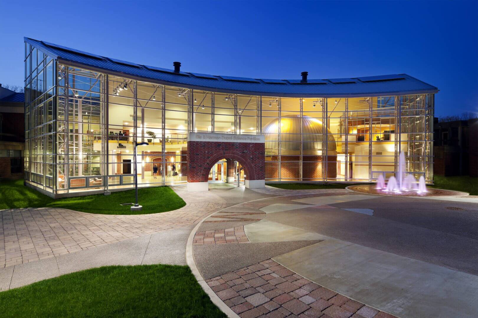 Modern glass building with curved architecture illuminated at dusk.