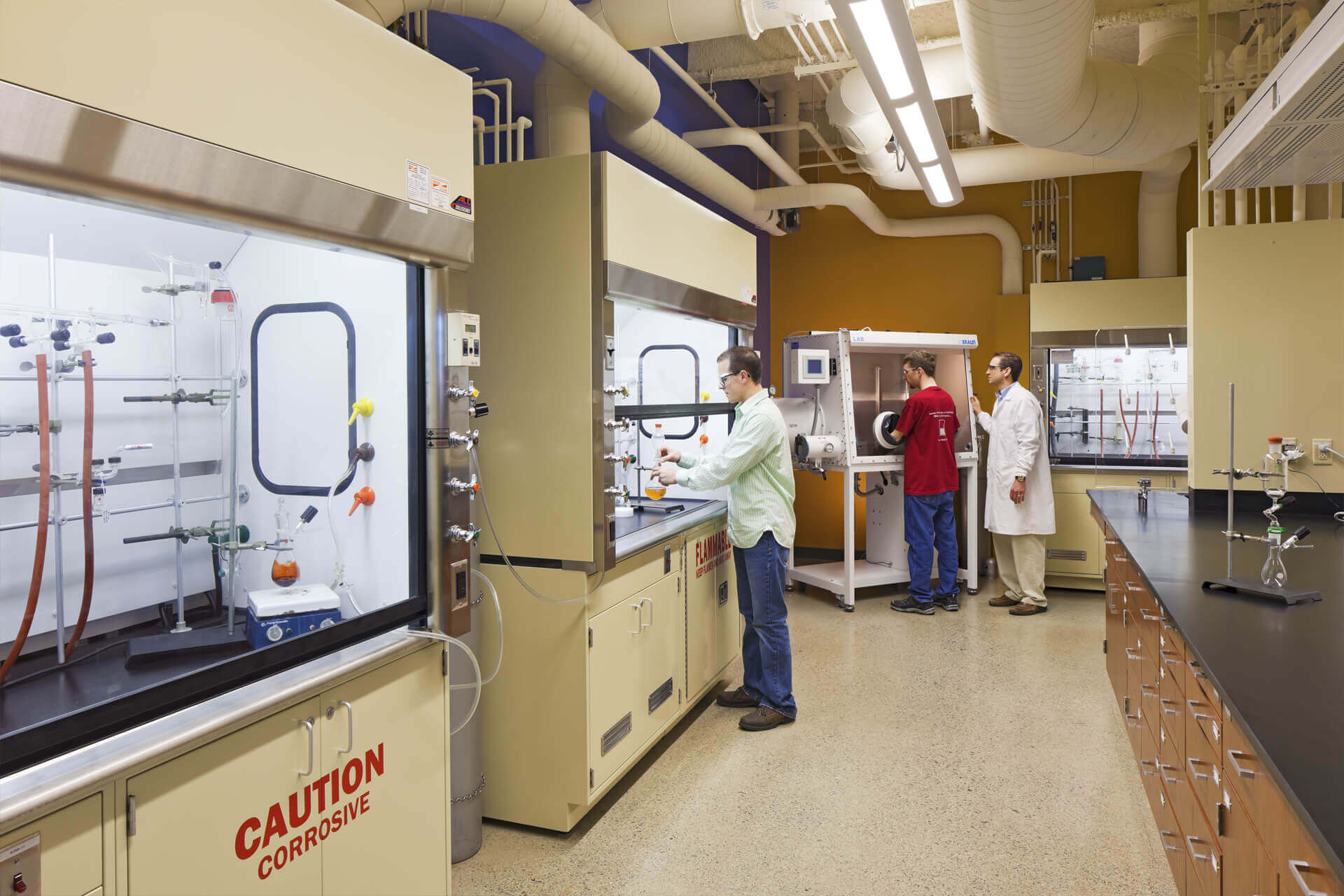 Scientists working in a chemistry lab with fume hoods and safety gear.