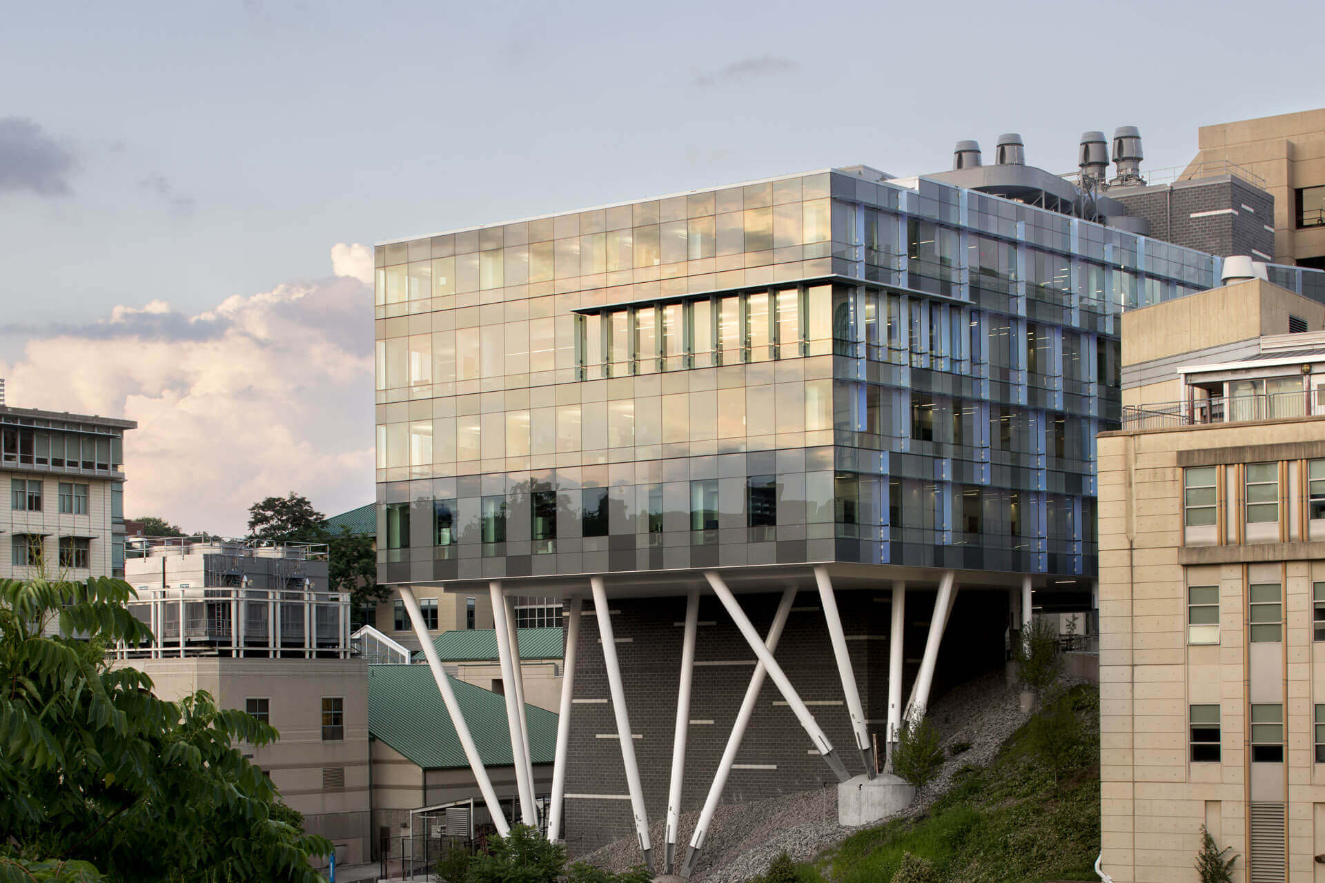 Modern glass building elevated on angled supports at sunset.