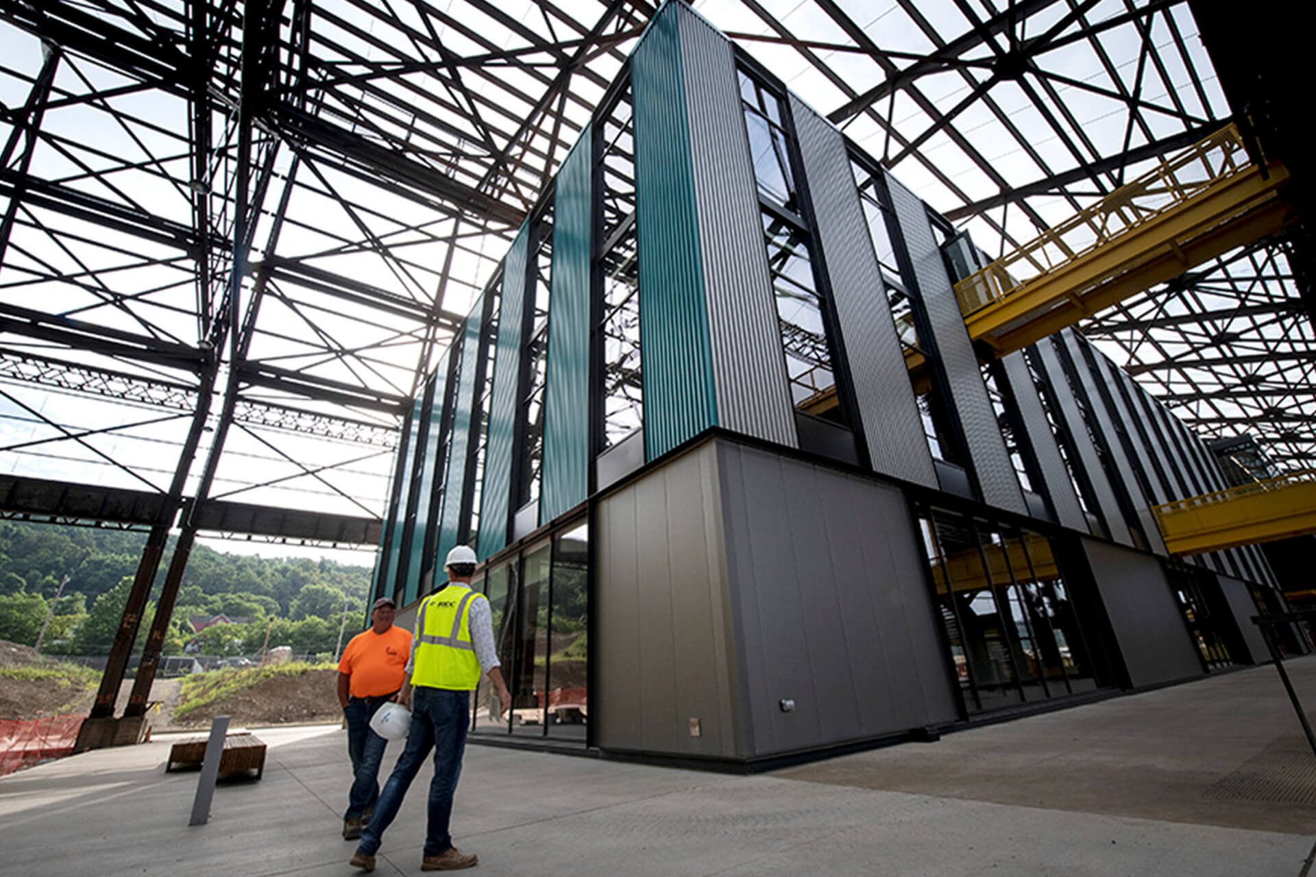 Two workers walk near a modern industrial building under construction.
