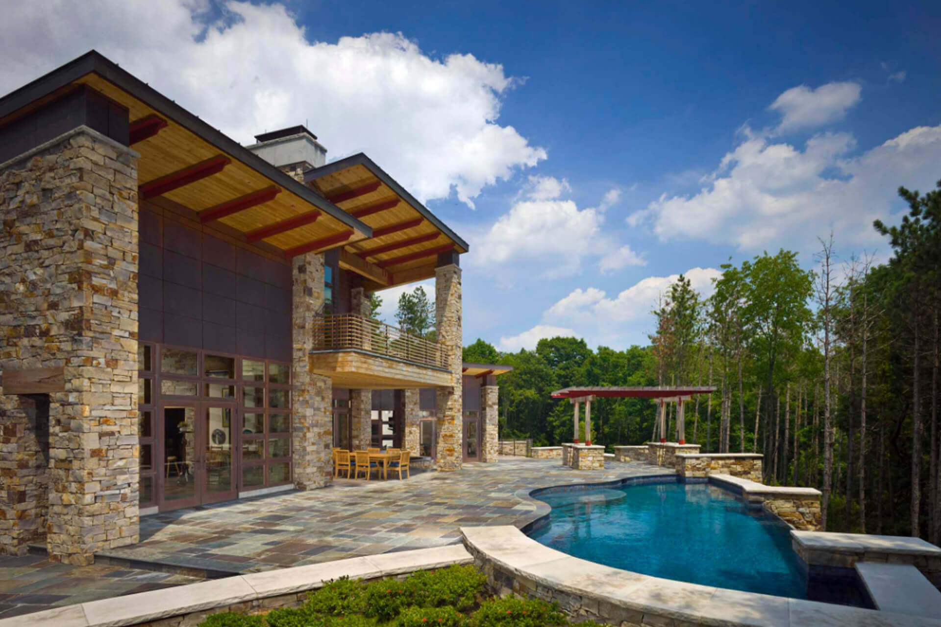 A stone house with a pool and patio under a blue sky.