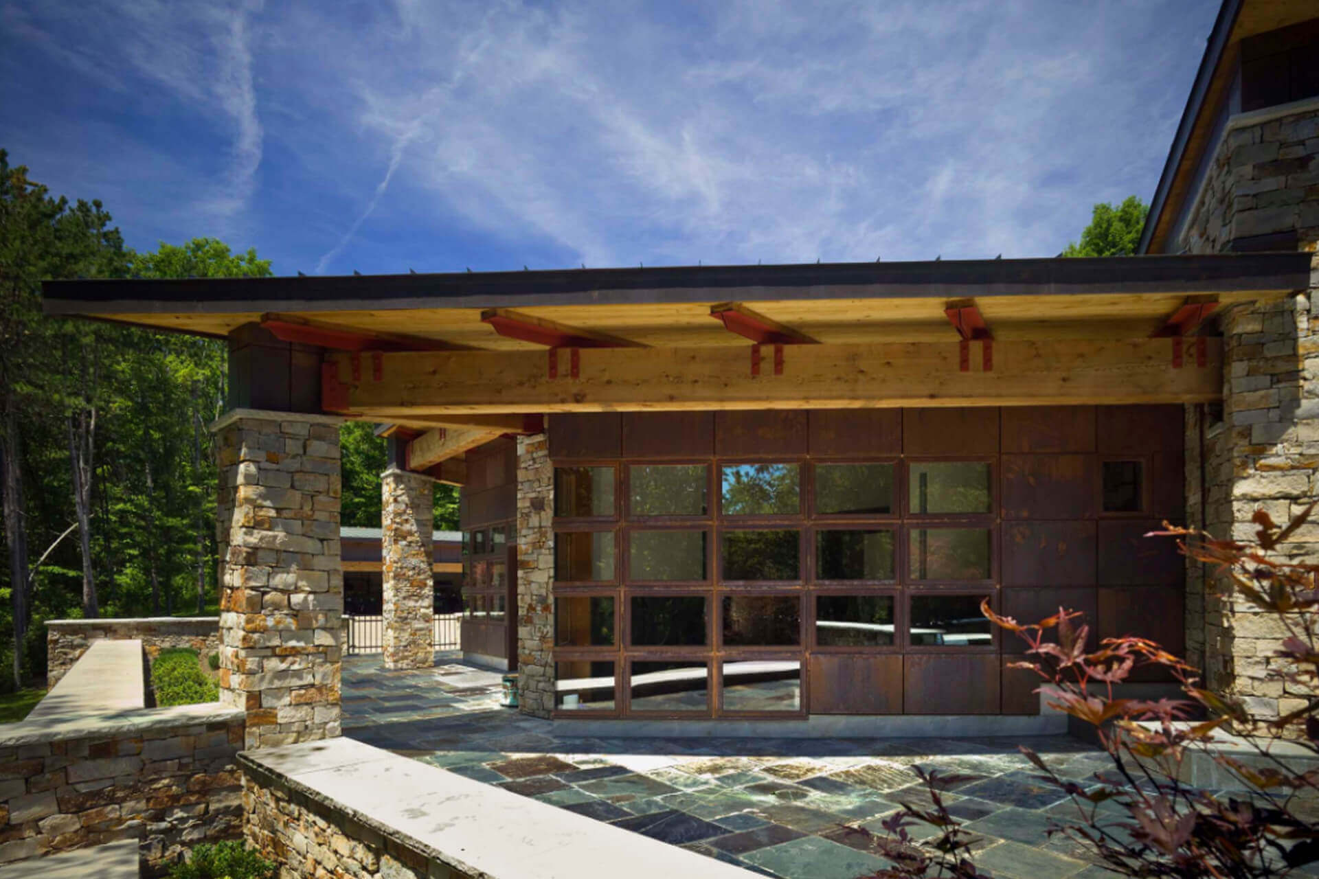 Modern house entrance with stone pillars and large glass door under a blue sky.