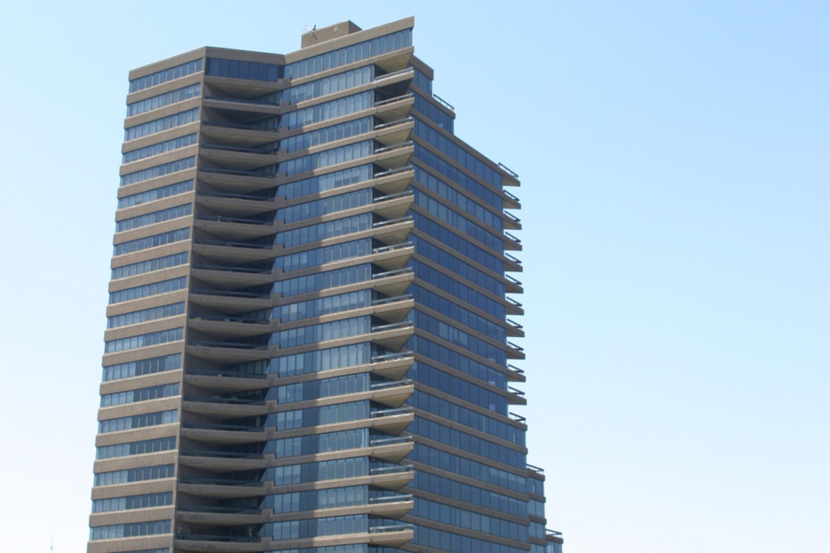 A tall modern building with many balconies under a clear blue sky.