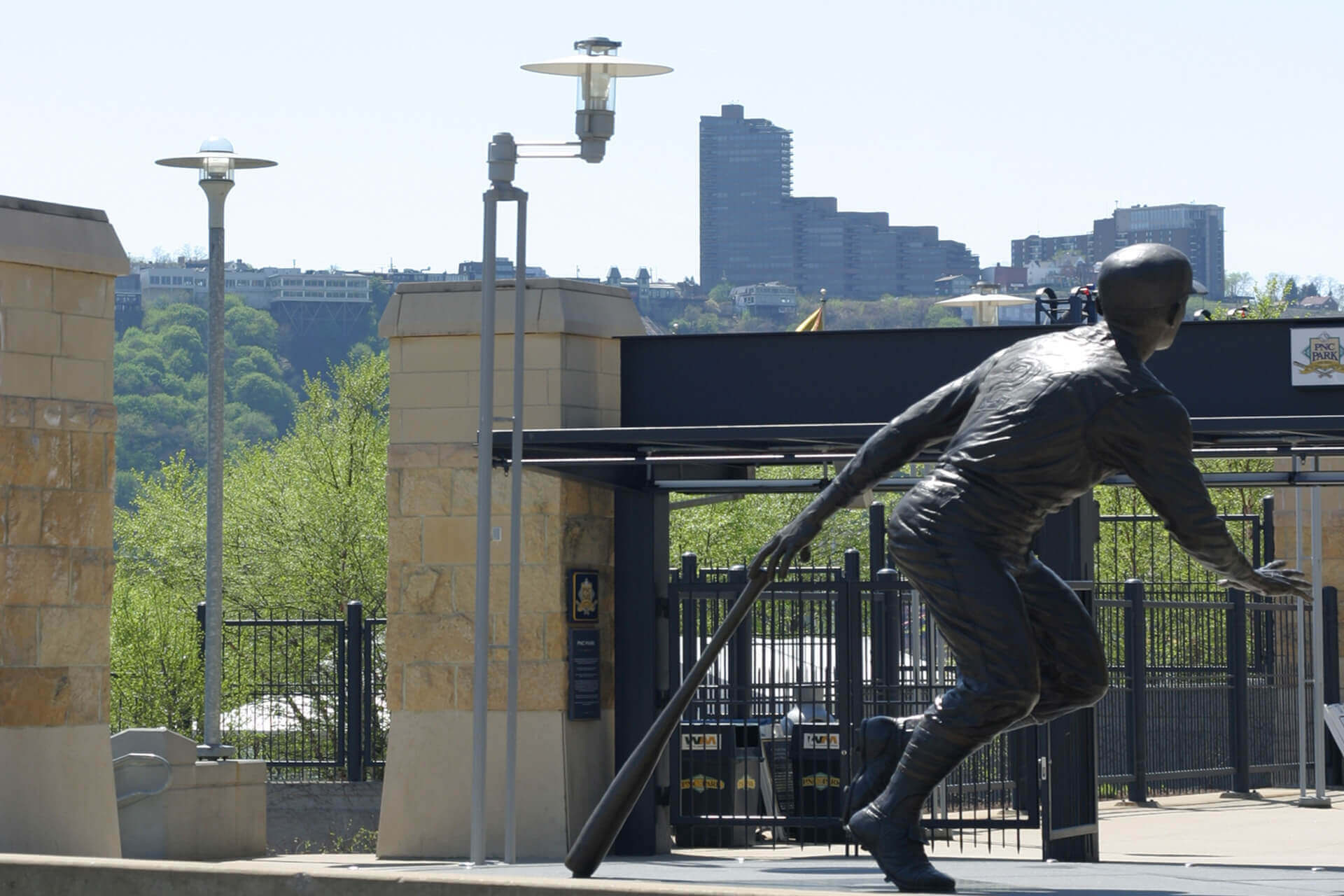 A sculpture of a baseball player near a stadium entrance with city buildings in the background.