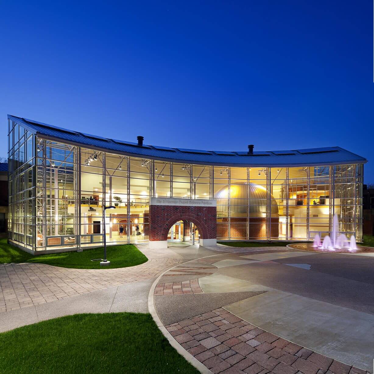 Curved glass building illuminated at dusk