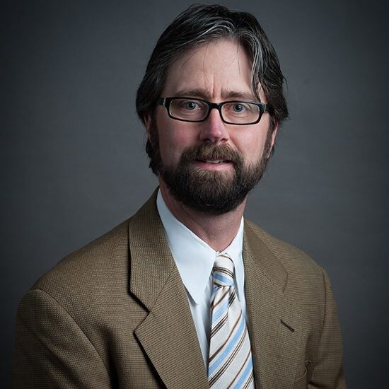 Man in suit with glasses and beard.