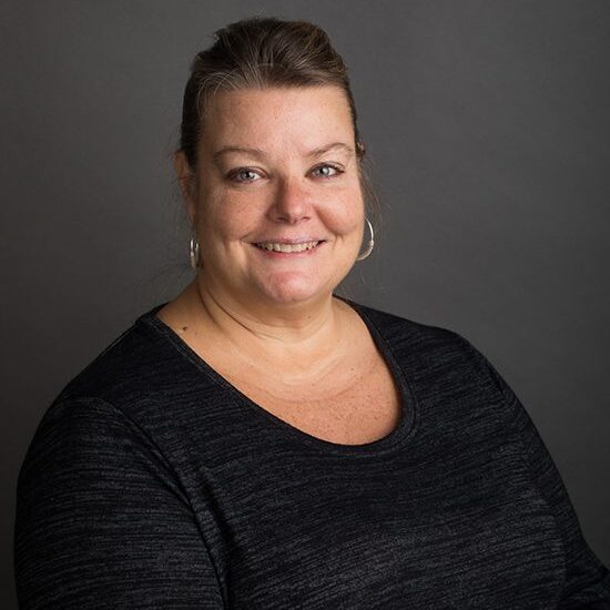 Smiling woman in dark shirt, gray background.