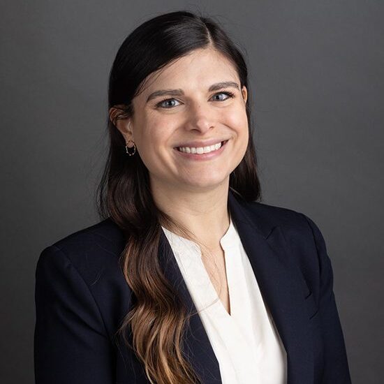 Smiling woman in business attire, dark background.