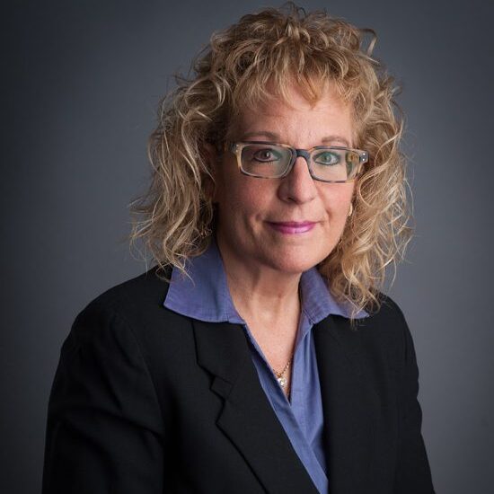 Woman in glasses with curly hair, suit.